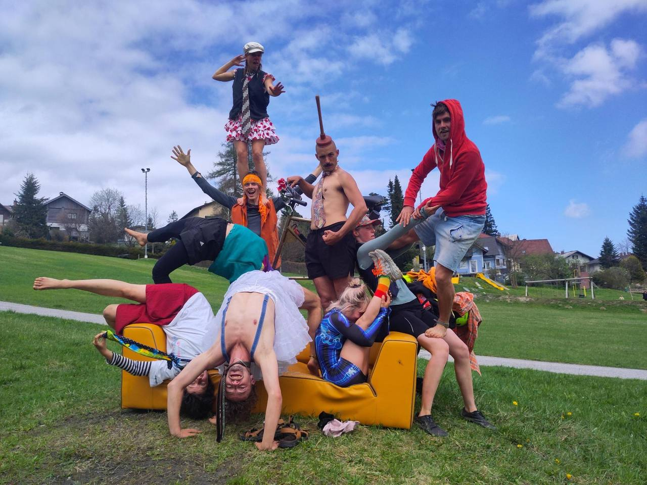 Fjollede cirkusartister der leger på en gul sofa i hvad der ligner en offentlig park